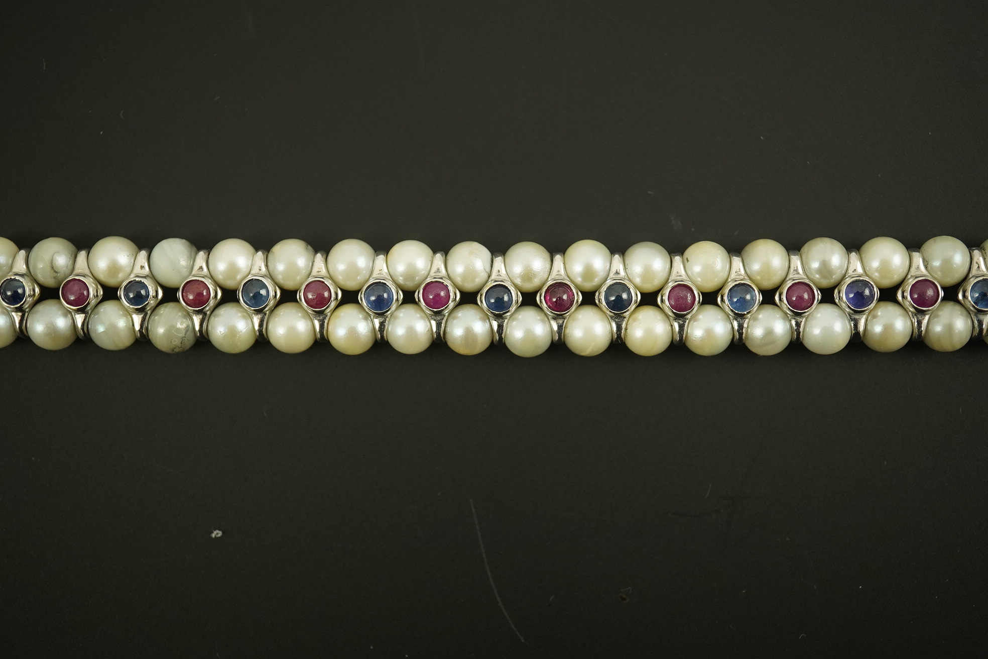 A late 20th century 18k white gold and two row cultured pearl bracelet, set with single row of cabochon rubies and sapphires